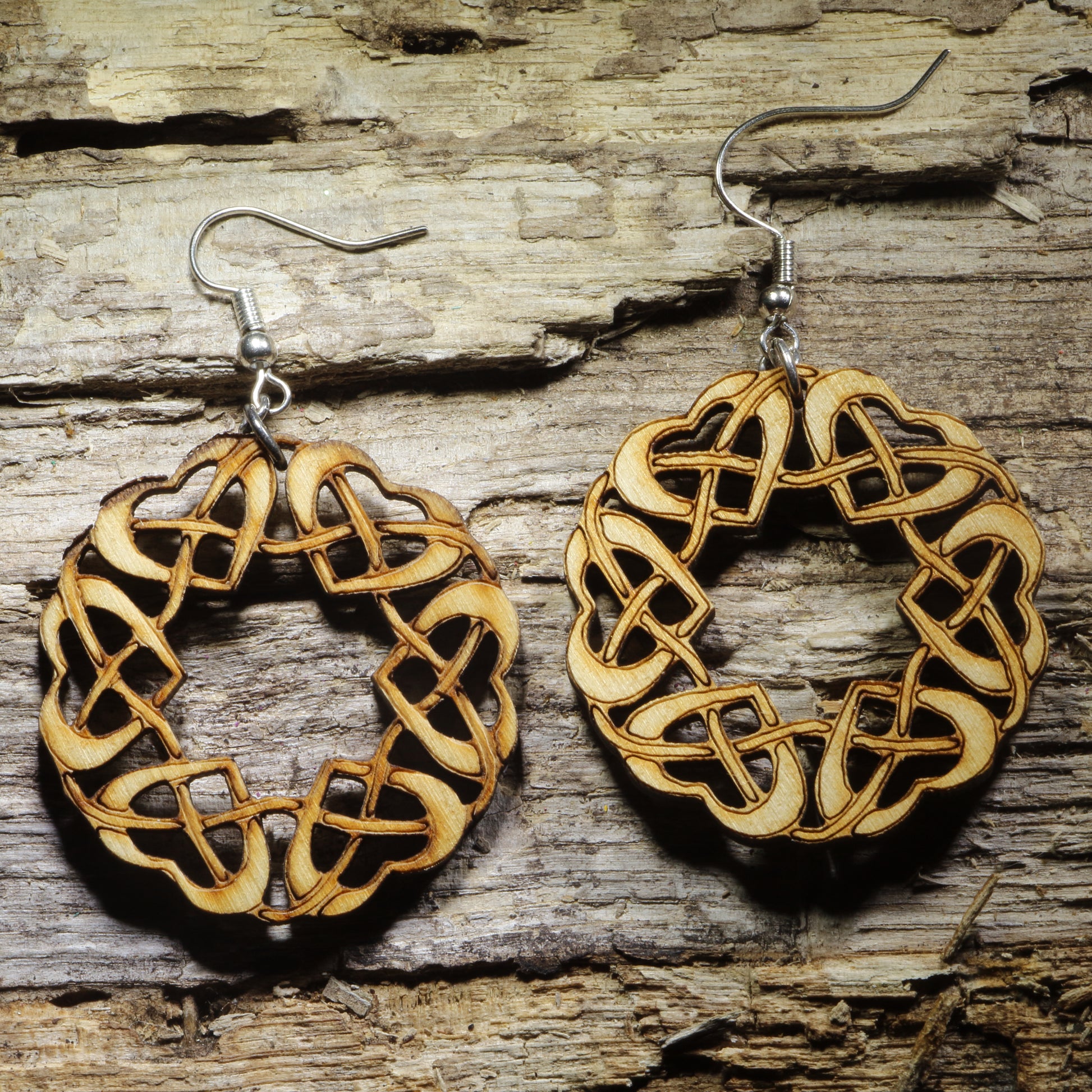 Pair of natural wood Celtic knot dangle earrings featuring an intricate circular interwoven heart pattern inspired by traditional Celtic jewelry, displayed on rustic weathered wood