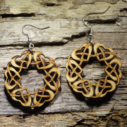 Pair of natural wood Celtic knot dangle earrings featuring an intricate circular interwoven heart pattern inspired by traditional Celtic jewelry, displayed on rustic weathered wood