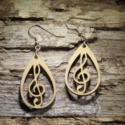 Pair of natural wood treble clef teardrop dangle earrings featuring an openwork musical note design displayed on rustic weathered wood