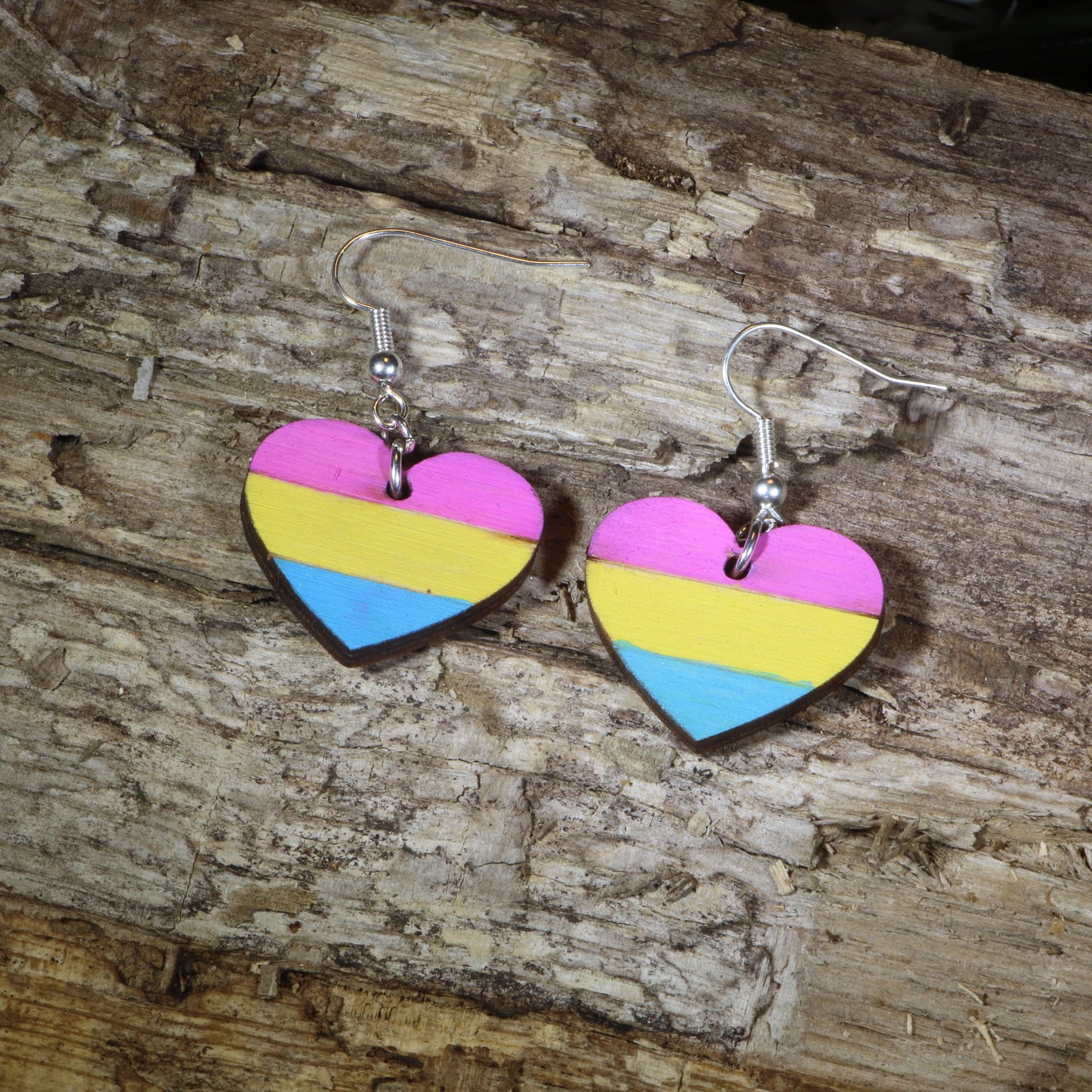 Hand-painted wooden pansexual heart dangle earrings featuring pink, yellow, and blue pansexual pride stripes, hypoallergenic sterling silver hooks, and lightweight LGBTQ+ pride jewelry for pansexual pride celebrations and queer accessory lovers by Cate's Concepts.