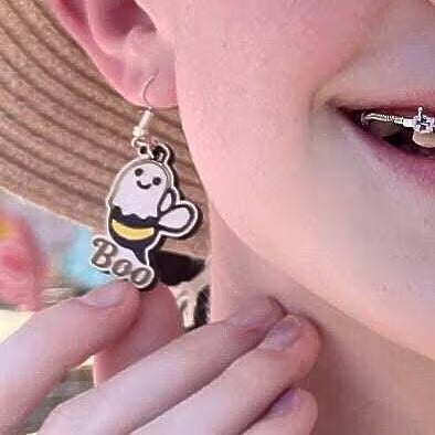 Person wearing hand-painted wooden "Boo Bees" dangle earrings on hypoallergenic .925 sterling silver hooks, showing the lightweight size, playful ghost bee design, and comfortable fit when worn.