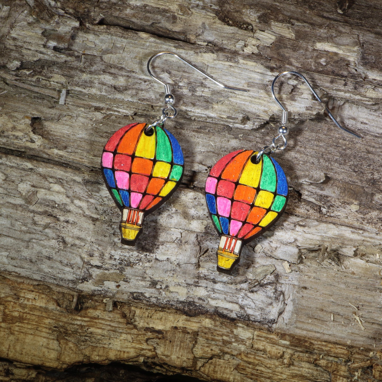 Hand-painted wooden rainbow hot air balloon dangle earrings featuring colorful stained-glass inspired balloon panels, hypoallergenic sterling silver hooks, and lightweight travel jewelry for adventure lovers, festival outfits, and rainbow accessory fans by Cate's Concepts.