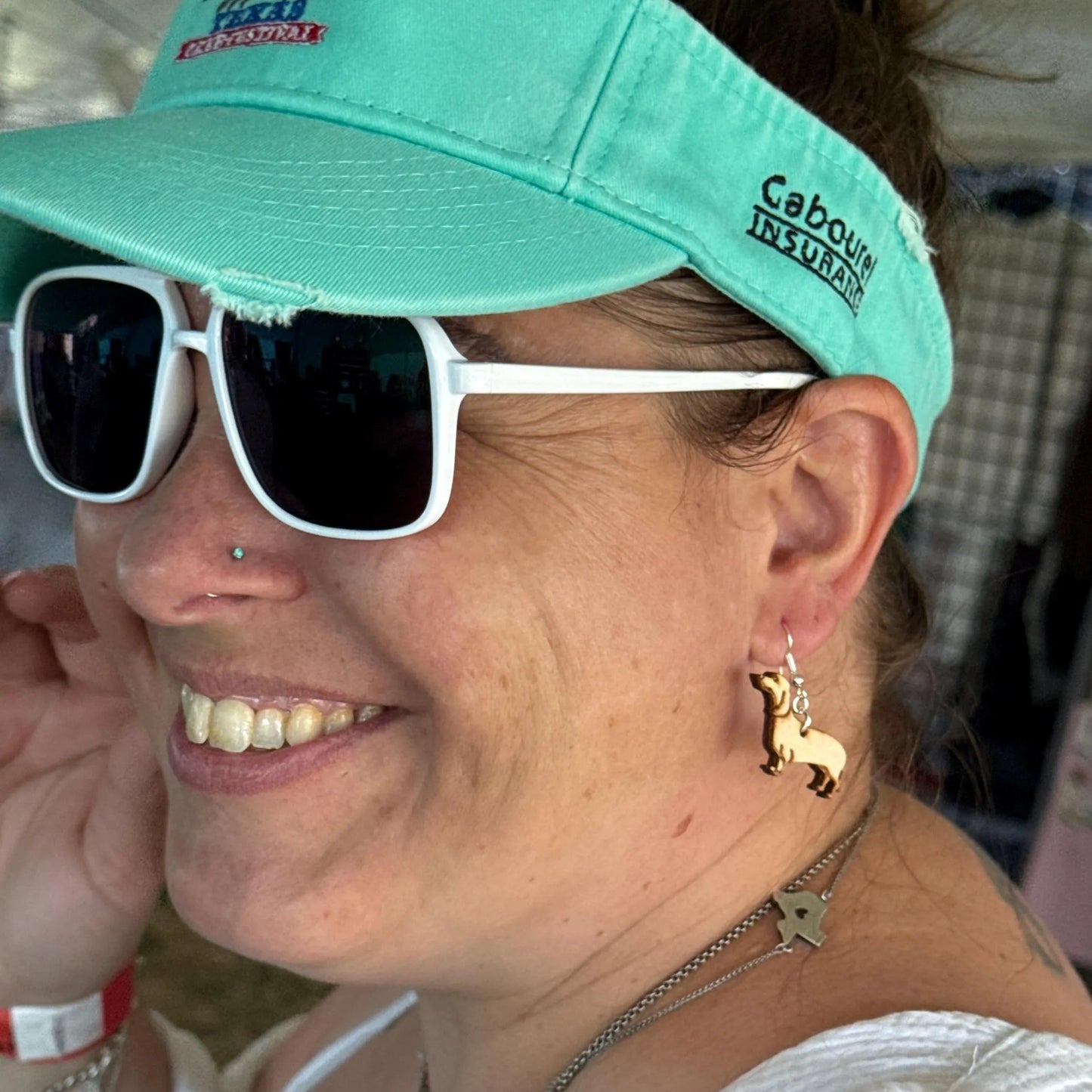Smiling customer wearing handmade wooden Dachshund dangle earrings crafted from lightweight wood with hypoallergenic .925 sterling silver hooks. Close-up showcases the adorable wiener dog design, ideal for Dachshund owners and dog lovers.