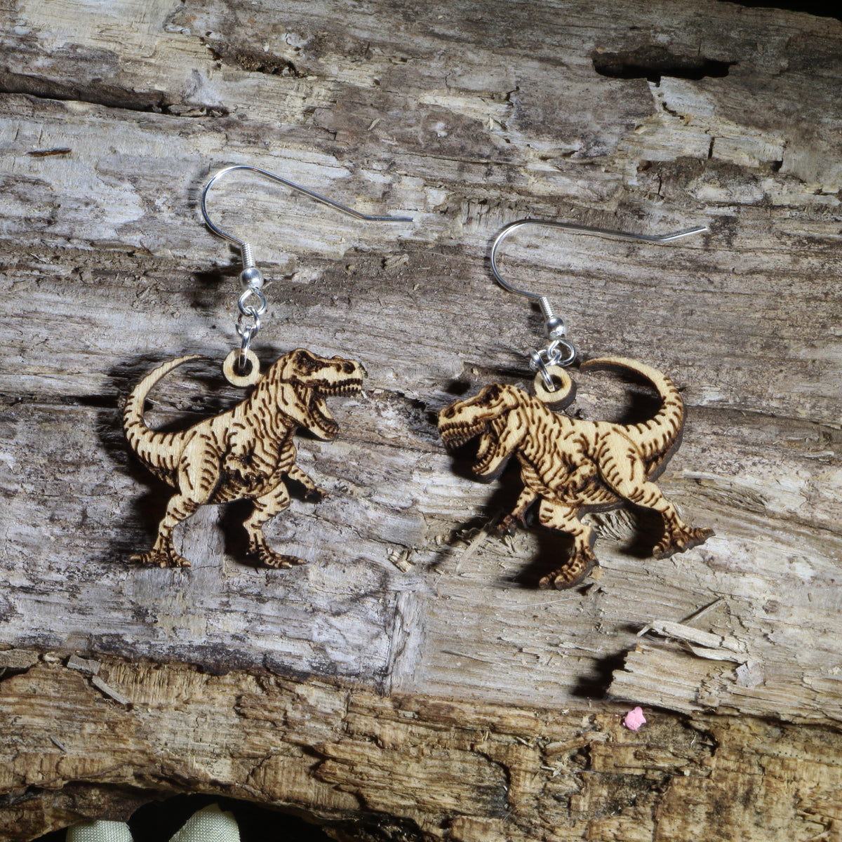T-Rex wooden dangle earrings featuring detailed Tyrannosaurus rex dinosaurs available in natural wood finishes. Lightweight dinosaur earrings with hypoallergenic .925 sterling silver hooks, perfect for dinosaur lovers, paleontology fans, science teachers, museum enthusiasts, and prehistoric-themed gifts.