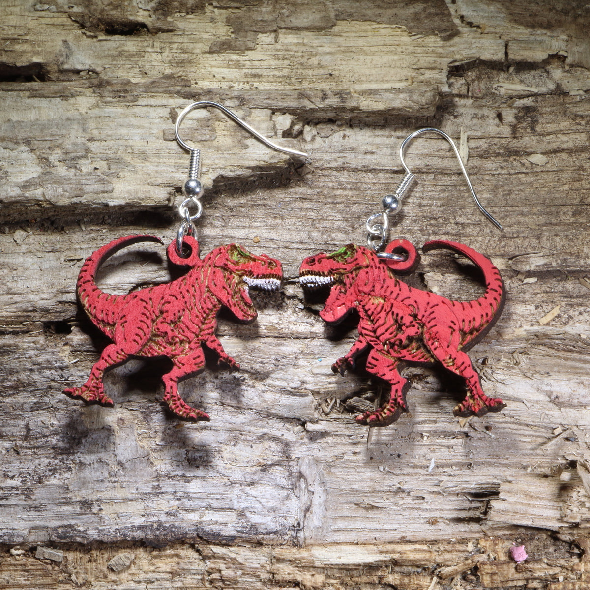T-Rex wooden dangle earrings featuring detailed Tyrannosaurus rex dinosaurs available in red finishes. Lightweight dinosaur earrings with hypoallergenic .925 sterling silver hooks, perfect for dinosaur lovers, paleontology fans, science teachers, museum enthusiasts, and prehistoric-themed gifts.