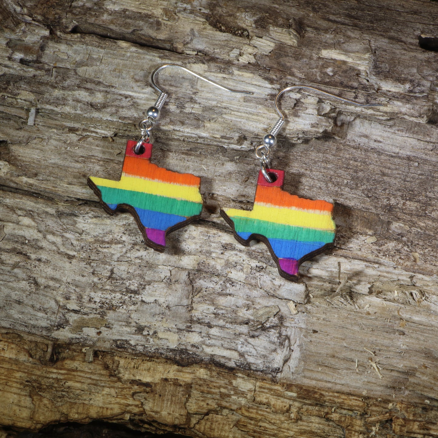 Hand-painted wooden Texas LGBTQ Pride dangle earrings featuring the Texas state silhouette with vibrant rainbow pride stripes, hypoallergenic sterling silver hooks, and lightweight LGBTQ+ state pride jewelry by Cate's Concepts.