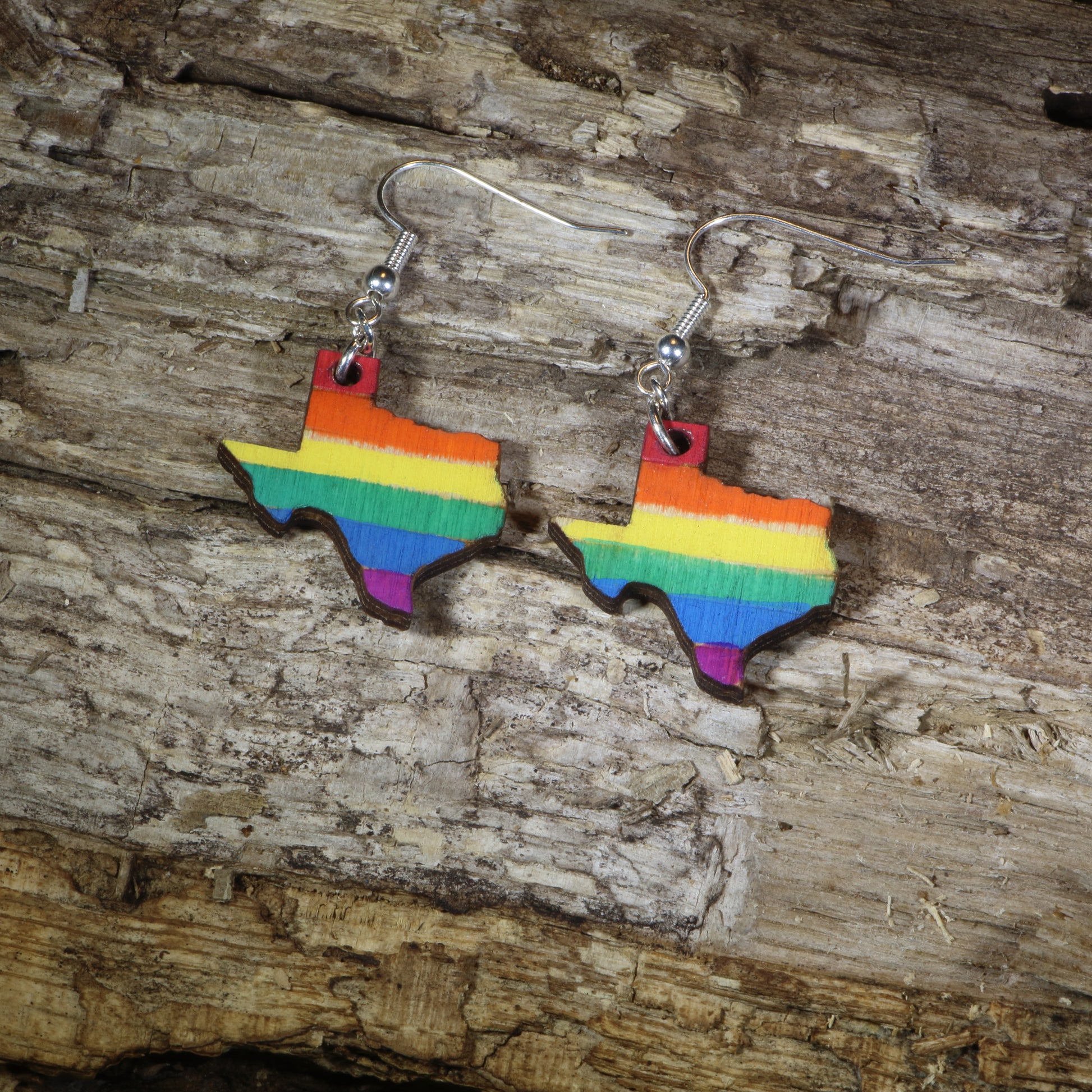 Hand-painted wooden Texas LGBTQ Pride dangle earrings featuring the Texas state silhouette with vibrant rainbow pride stripes, hypoallergenic sterling silver hooks, and lightweight LGBTQ+ state pride jewelry by Cate's Concepts.