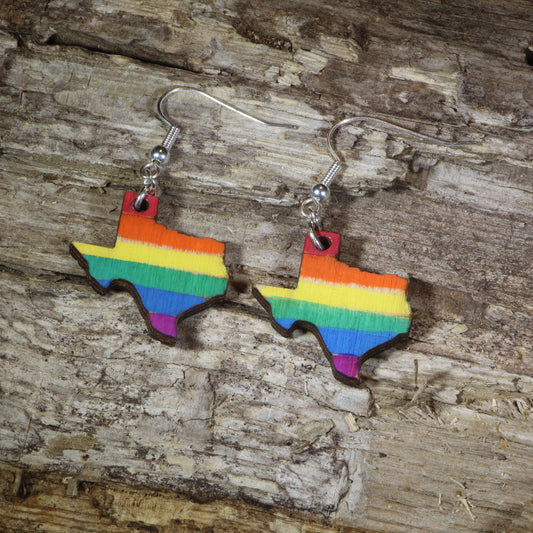 Hand-painted wooden Texas LGBTQ Pride dangle earrings featuring the Texas state silhouette with vibrant rainbow pride stripes, hypoallergenic sterling silver hooks, and lightweight LGBTQ+ state pride jewelry by Cate's Concepts.