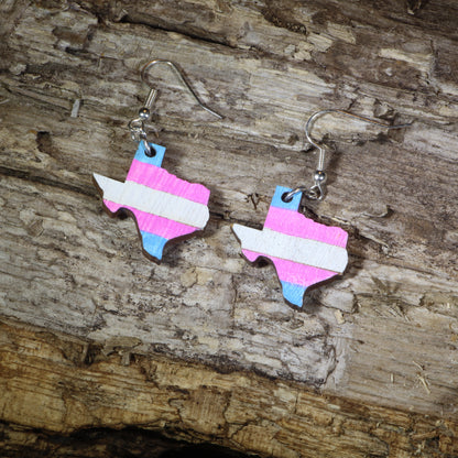 Hand-painted wooden Texas transgender pride dangle earrings featuring the Texas state silhouette with pink, blue, and white transgender pride stripes, hypoallergenic sterling silver hooks, and lightweight LGBTQ+ state pride jewelry by Cate's Concepts.