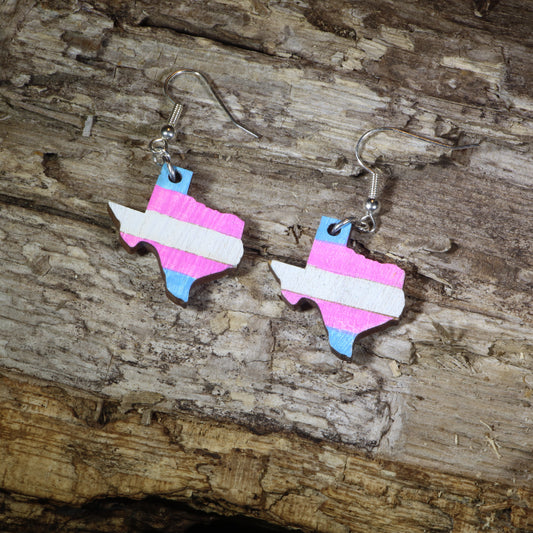 Hand-painted wooden Texas transgender pride dangle earrings featuring the Texas state silhouette with pink, blue, and white transgender pride stripes, hypoallergenic sterling silver hooks, and lightweight LGBTQ+ state pride jewelry by Cate's Concepts.