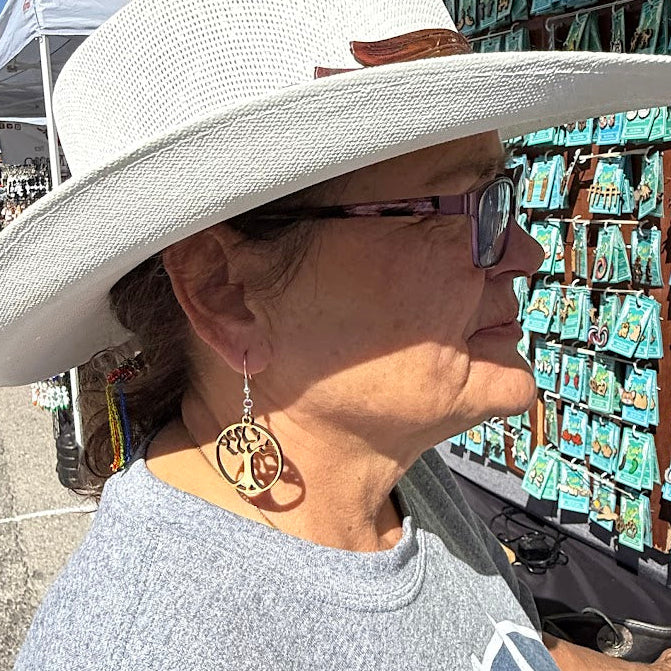 Lifestyle photo of woman wearing hand-painted wooden tree of life dangle earrings with hypoallergenic sterling silver hooks, nature-inspired statement jewelry at outdoor market