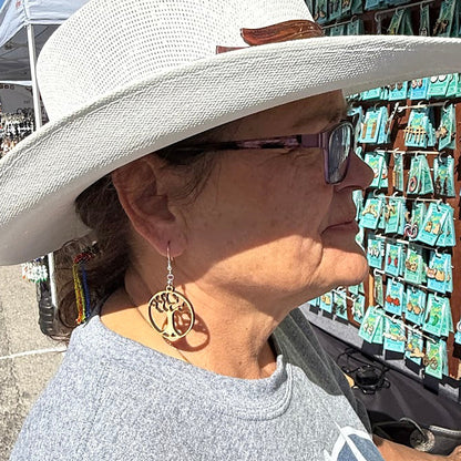 Lifestyle photo of woman wearing hand-painted wooden tree of life dangle earrings with hypoallergenic sterling silver hooks, nature-inspired statement jewelry at outdoor market