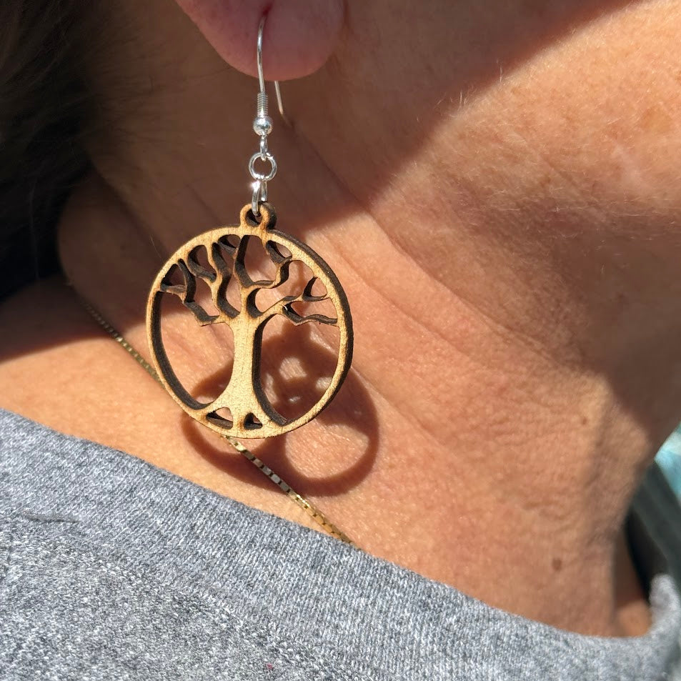 Close-up of hand-painted wooden Tree of Life Wooden Earrings with circular cutout design and hypoallergenic sterling silver hook, lightweight nature-inspired jewelry worn on ear