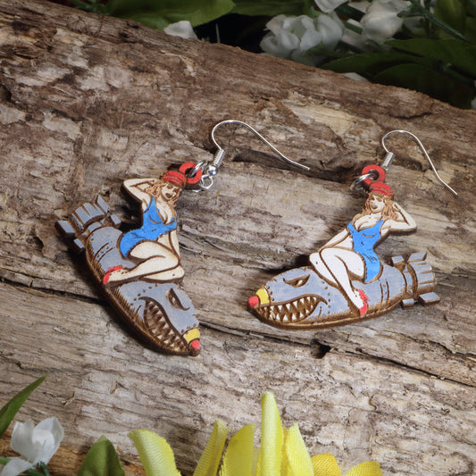 Hand-painted wooden bomber girl dangle earrings featuring a vintage pin-up riding a shark-mouth bomber design, hypoallergenic sterling silver hooks, and lightweight retro military-inspired jewelry for aviation enthusiasts and WWII nostalgia lovers by Cate’s Concepts.
