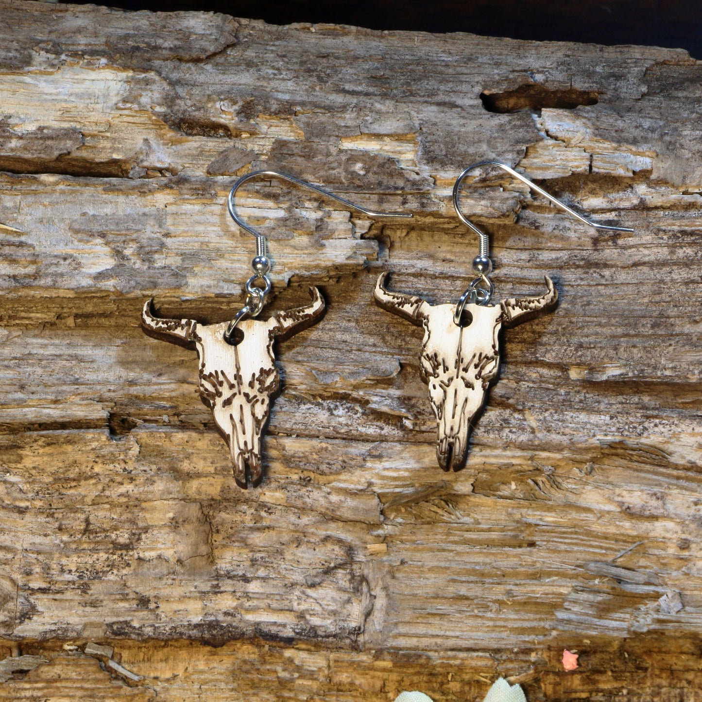 Hand-painted wooden longhorn cattle skull dangle earrings featuring a detailed western cow skull with curved horns inspired by the American Southwest. Crafted from lightweight wood with hypoallergenic .925 sterling silver hooks, these rustic earrings are perfect for western fashion, rodeo fans, ranch life, cowgirl style, country music festivals, Texas pride, and anyone who loves southwestern-inspired jewelry.