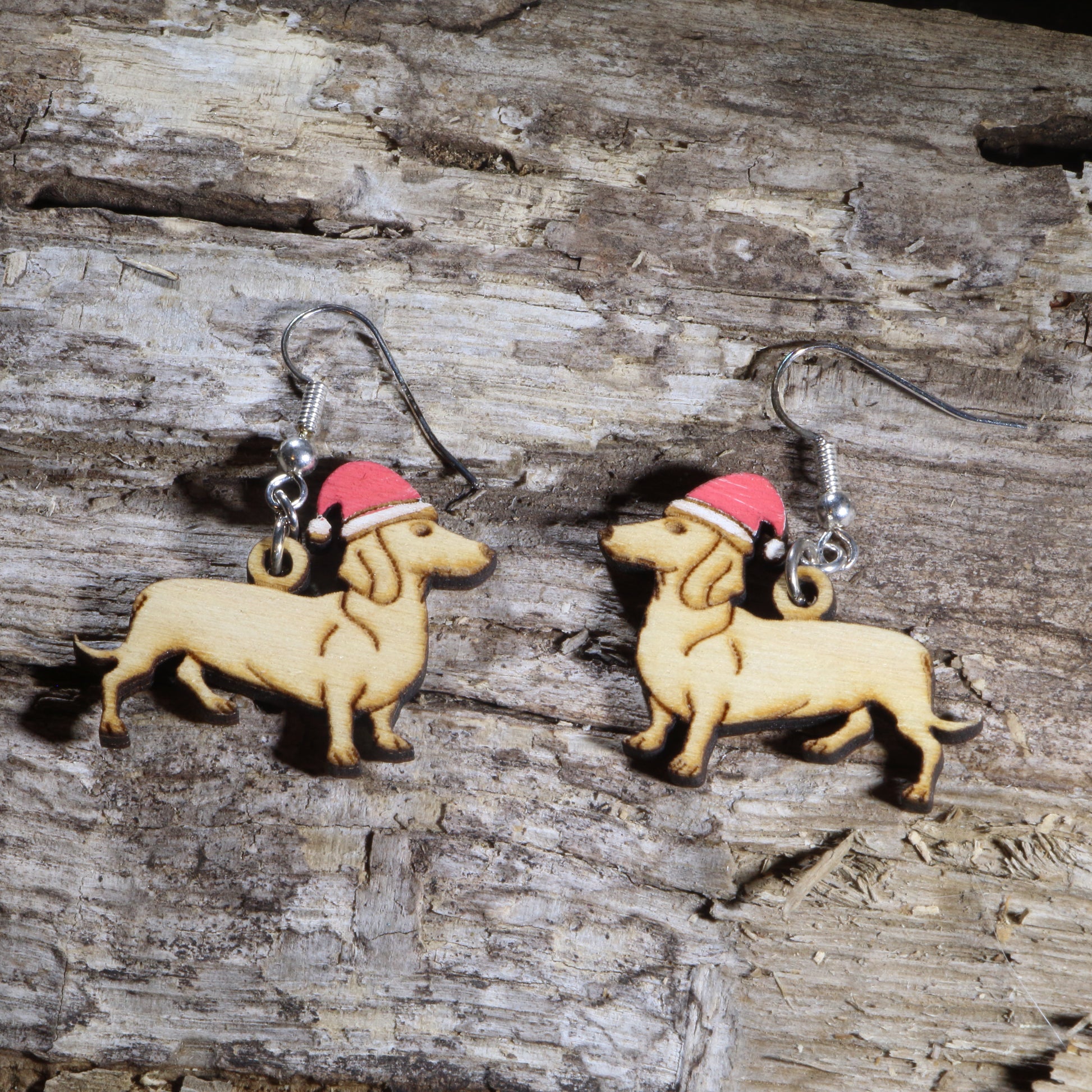 Hand-painted wooden Dachshund dangle earrings featuring an adorable wiener dog wearing a festive Santa hat. Crafted from lightweight wood with hypoallergenic .925 sterling silver hooks, these charming holiday earrings are perfect for Dachshund lovers, dog moms, Christmas parties, holiday markets, festive winter outfits, pet lovers, and anyone who enjoys whimsical Christmas jewelry.