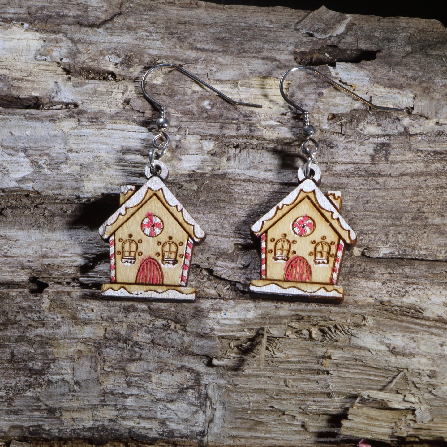 Hand-painted wooden gingerbread house dangle earrings featuring a charming holiday cottage decorated with candy cane trim, peppermint candy windows, snowy icing details, and a festive Christmas design. Crafted from lightweight wood with hypoallergenic .925 sterling silver hooks, these whimsical earrings are perfect for Christmas parties, holiday baking, winter festivals, cookie exchange gifts, Christmas market shopping, and anyone who loves festive holiday jewelry.