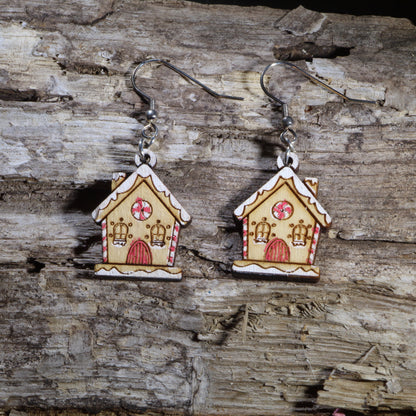 Hand-painted wooden gingerbread house dangle earrings featuring a charming holiday cottage decorated with candy cane trim, peppermint candy windows, snowy icing details, and a festive Christmas design. Crafted from lightweight wood with hypoallergenic .925 sterling silver hooks, these whimsical earrings are perfect for Christmas parties, holiday baking, winter festivals, cookie exchange gifts, Christmas market shopping, and anyone who loves festive holiday jewelry.