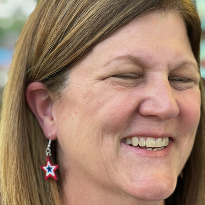 Person wearing hand-painted patriotic star wooden dangle earring on a hypoallergenic .925 sterling silver hook, showing the lightweight size and fit when worn. Red, white, and blue star jewelry perfect for patriotic celebrations, Independence Day, Memorial Day, and everyday American pride.