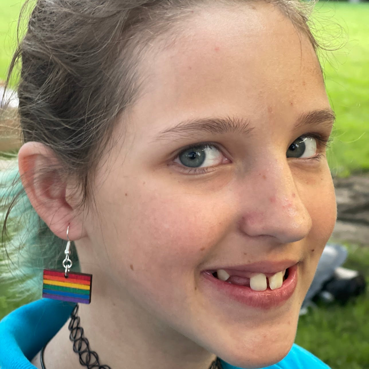 Person wearing hand-painted wooden LGBTQ+ Pride flag dangle earring on a hypoallergenic .925 sterling silver hook, showing the lightweight size and fit when worn. Rainbow Pride jewelry celebrating LGBTQ+ pride, equality, inclusion, and self-expression.