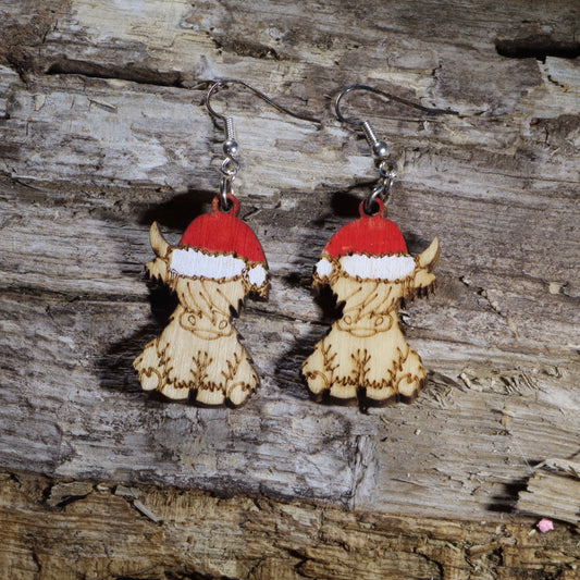 Hand-painted wooden Highland cow dangle earrings featuring an adorable fluffy Highland calf wearing a festive red and white Santa hat. Crafted from lightweight wood with hypoallergenic .925 sterling silver hooks, these charming Christmas earrings are perfect for Highland cow lovers, farm animal enthusiasts, holiday parties, winter celebrations, stocking stuffers, and anyone who loves rustic Christmas jewelry with cozy country charm.