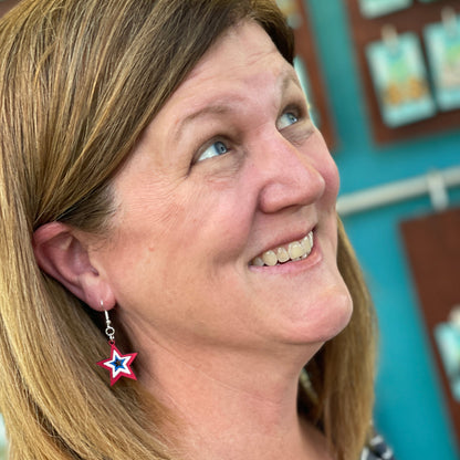 Person wearing hand-painted patriotic star wooden dangle earring on a hypoallergenic .925 sterling silver hook, showing the lightweight size and fit when worn. Red, white, and blue star jewelry for Fourth of July celebrations, military families, veterans, and patriotic style.