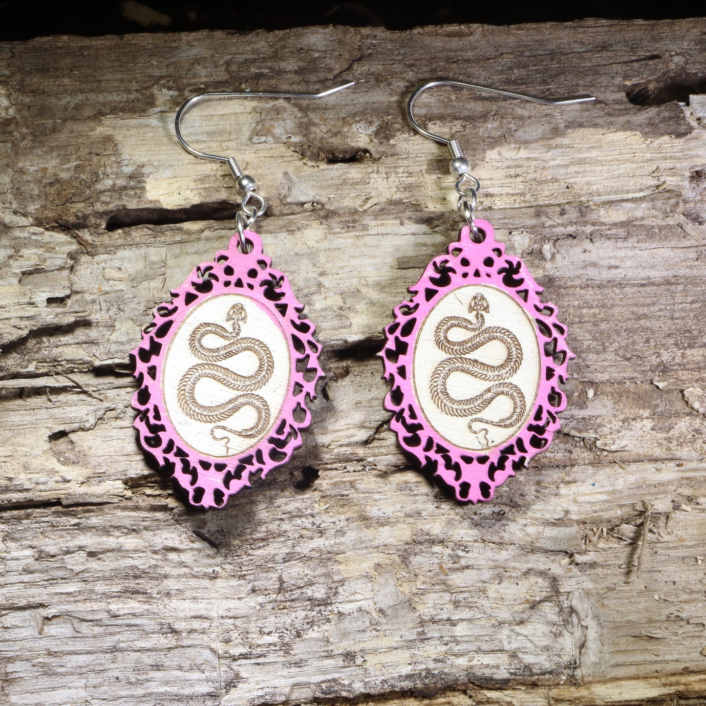 Handcrafted pink framed snake wooden dangle earrings featuring a detailed serpent coiled within an ornate gothic-inspired frame. Lightweight laser-cut wooden earrings with hypoallergenic .925 sterling silver hooks, perfect for snake lovers, gothic fashion, reptile enthusiasts, witchy style, dark academia, and nature-inspired handmade jewelry.