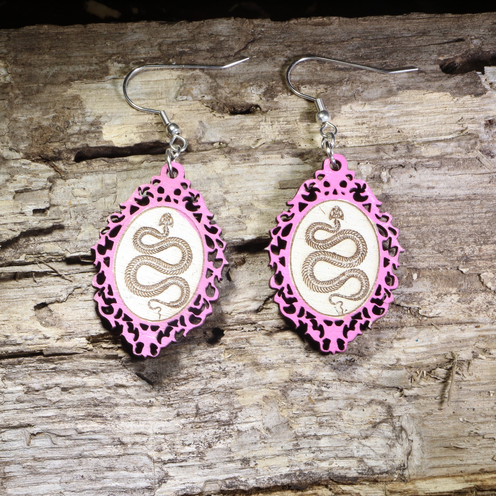 Handcrafted pink framed snake wooden dangle earrings featuring a detailed serpent coiled within an ornate gothic-inspired frame. Lightweight laser-cut wooden earrings with hypoallergenic .925 sterling silver hooks, perfect for snake lovers, gothic fashion, reptile enthusiasts, witchy style, dark academia, and nature-inspired handmade jewelry.