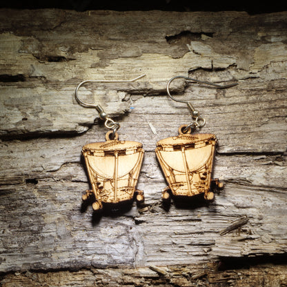 Pair of natural wood timpani kettle drum dangle earrings with detailed percussion instrument design displayed on rustic weathered wood