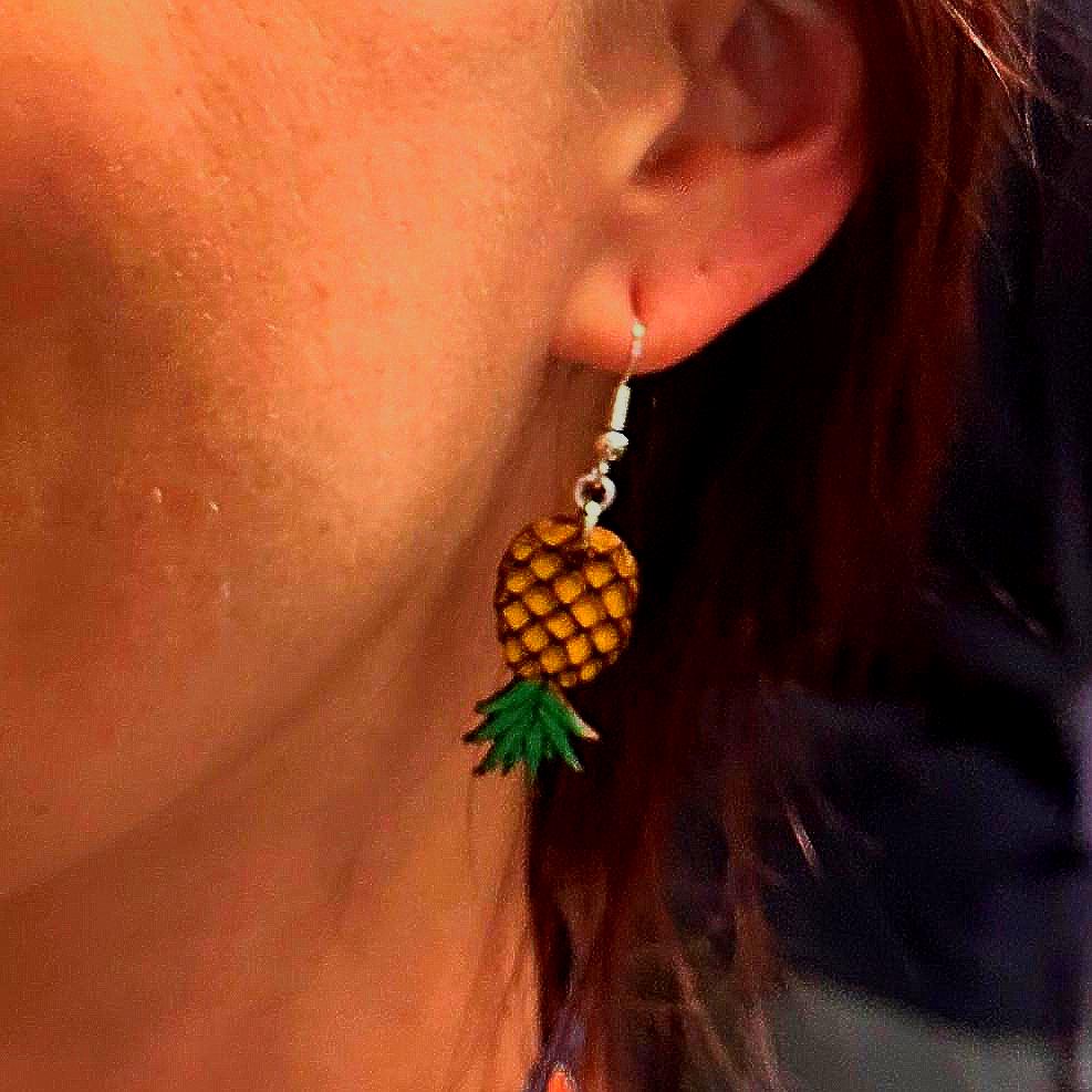 Close-up of a model wearing hand-painted wooden upside-down pineapple dangle earrings. The lightweight earrings with hypoallergenic .925 sterling silver hooks show their comfortable size and tropical charm, making them perfect for everyday wear, beach vacations, cruises, and summer outfits.