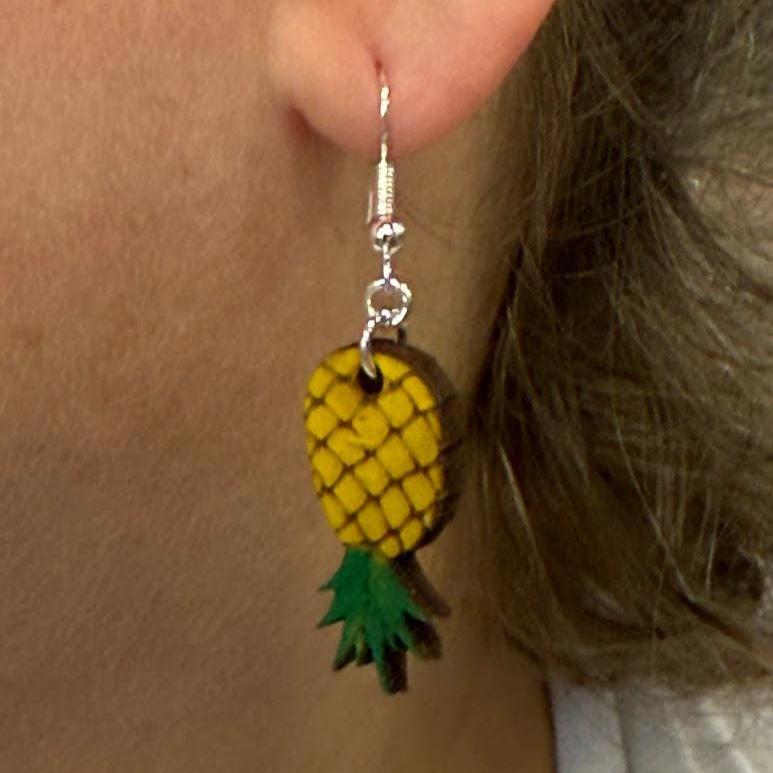 Detailed side profile highlighting the size and fit of the hand-painted wooden upside-down pineapple earrings. This close-up showcases the vibrant yellow and green colors, lightweight design, and hypoallergenic .925 sterling silver hooks for comfortable all-day wear.