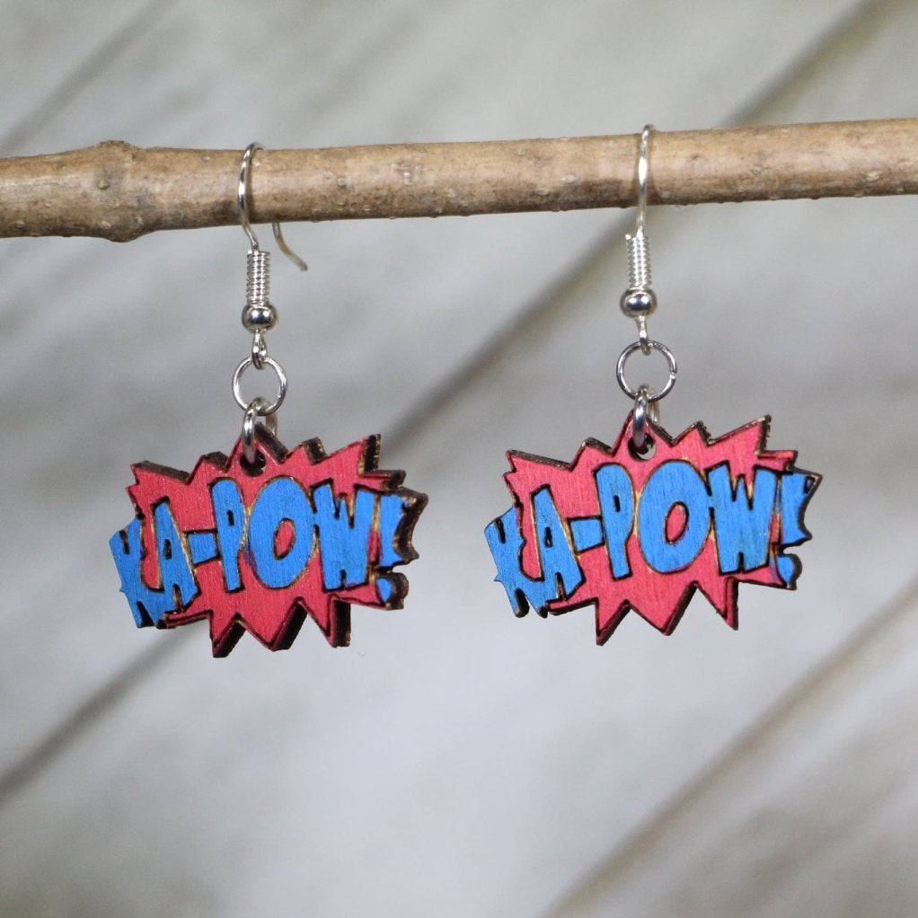 Hand-painted wooden KA-POW sound effect dangle earrings featuring a bold comic book explosion design with dynamic lettering and starburst detail and hypoallergenic sterling silver hooks, lightweight jewelry for pop art fans and comic lovers by Cate’s Concepts
