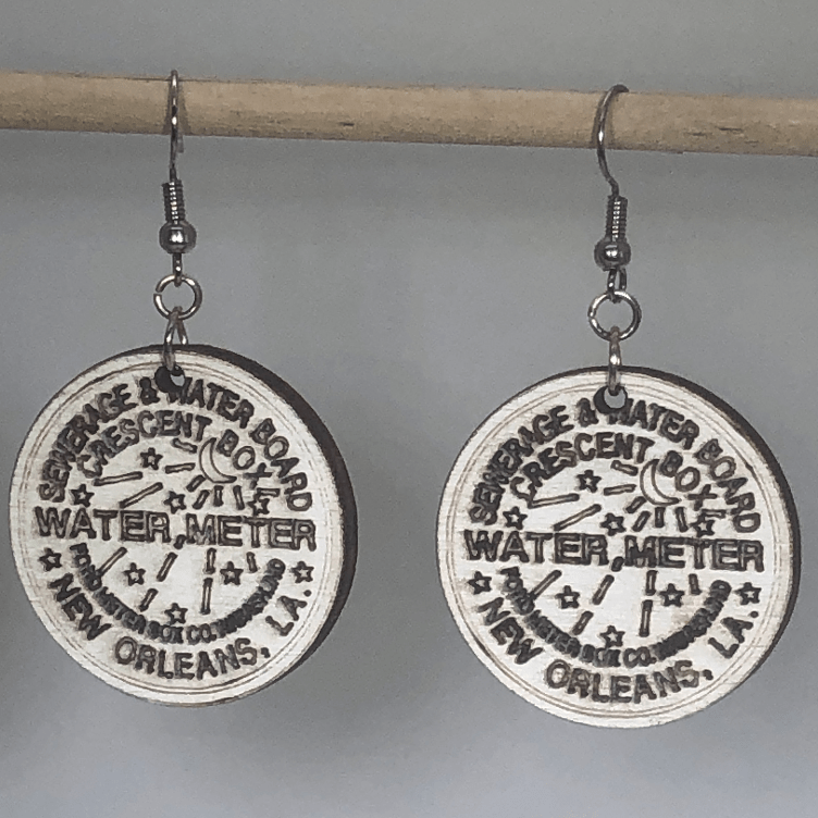 Hand-painted wooden New Orleans water meter dangle earrings featuring a detailed NOLA utility cover design with bold lettering and circular pattern and hypoallergenic sterling silver hooks, lightweight jewelry for New Orleans locals and city pride enthusiasts by Cate’s Concepts