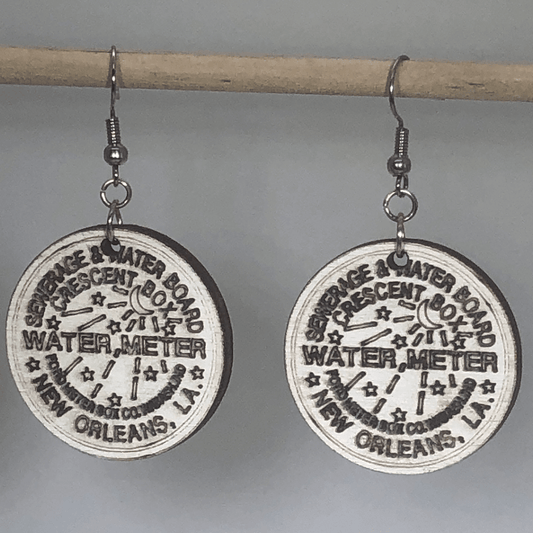 Hand-painted wooden New Orleans water meter dangle earrings featuring a detailed NOLA utility cover design with bold lettering and circular pattern and hypoallergenic sterling silver hooks, lightweight jewelry for New Orleans locals and city pride enthusiasts by Cate’s Concepts