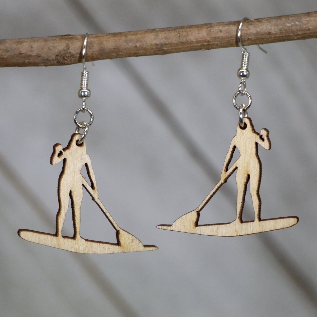 Hand-painted wooden paddle boarder dangle earrings featuring a silhouette of a stand-up paddler on a board with waterline detail and hypoallergenic sterling silver hooks, lightweight jewelry for water sports lovers and lake day enthusiasts by Cate’s Concepts