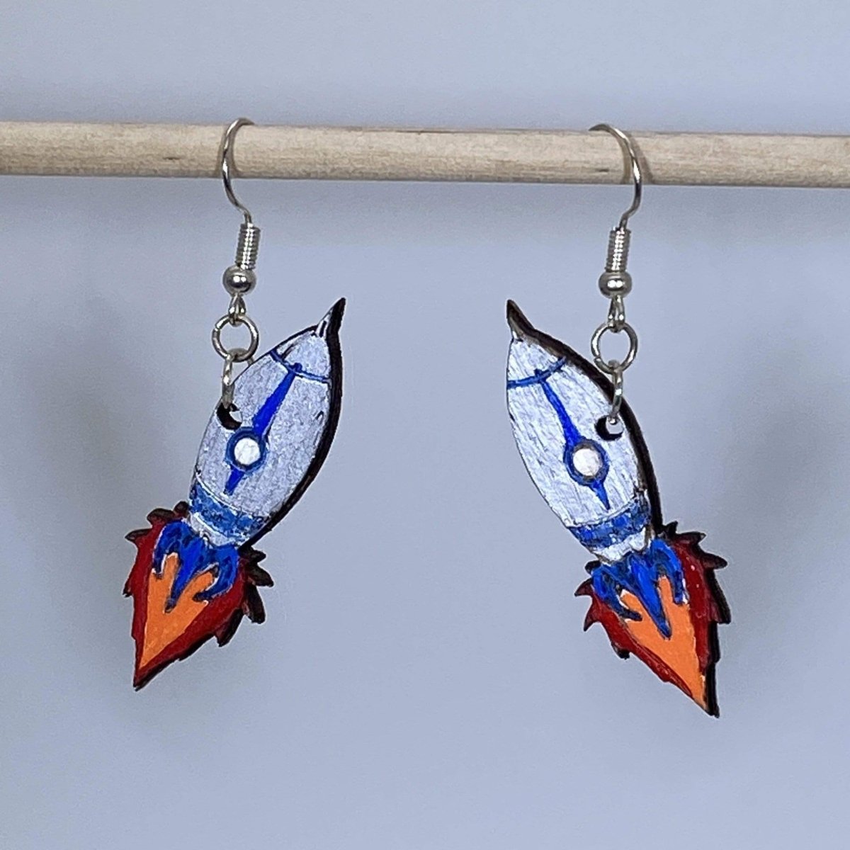 Hand-painted wooden rocket dangle earrings featuring a sleek space rocket design with pointed nose cone and flame details and hypoallergenic sterling silver hooks, lightweight jewelry for space enthusiasts and sci-fi fans by Cate’s Concepts